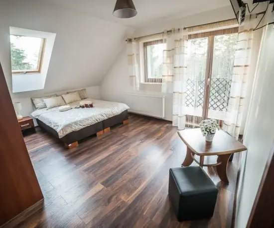 Grafika Světlý podkrovní pokoj s postelí, okny a malým stolkem – hotel Dolce Vita